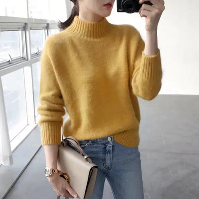 Person wearing a yellow sweater and blue jeans, holding a beige handbag indoors.