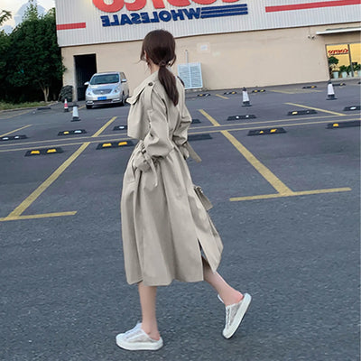 Woman in a trench coat walking in a parking lot with a store in the background