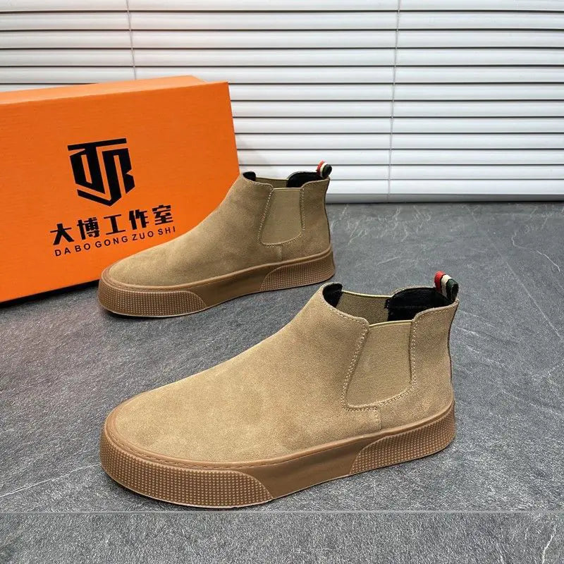 Brown Chelsea boots in front of an orange box with a brand logo on a gray floor.