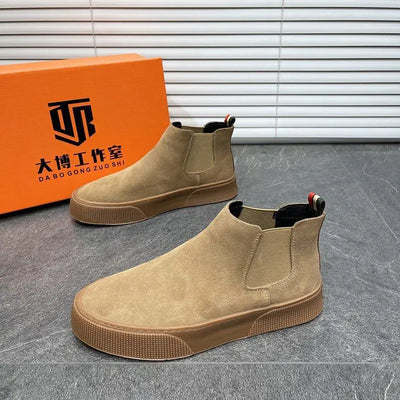 Brown Chelsea boots in front of an orange box with a brand logo on a gray floor.