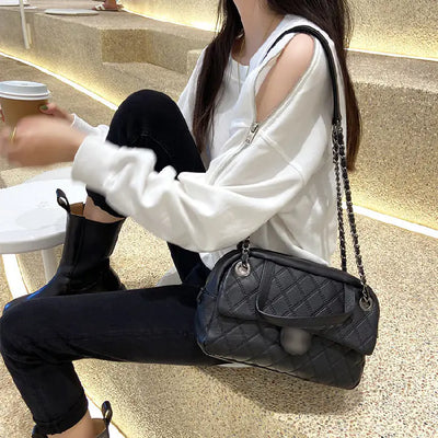Person sitting outdoors holding a coffee cup and a black quilted handbag.